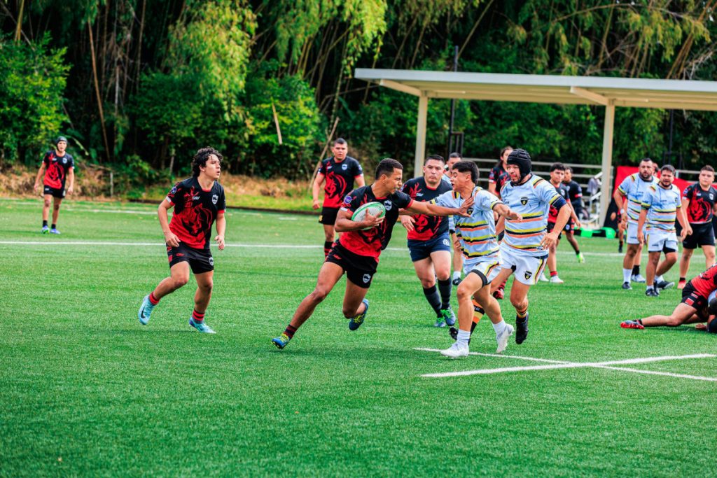 Action-packed rugby game on a sunny day with players in red and black jerseys.